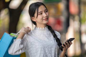 Asian woman in modern dress holding shopping bags walking outside a shopping mall.