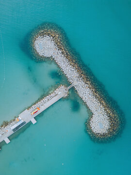 Aerial view of port des sablettes with tranquil turquoise water and rocky breakwater, Menton, France.