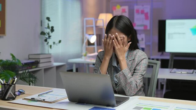 Asian businesswoman stressed and tired from work sitting at desk in office with pile of paperwork assigned by supervisor. Feel uncomfortable Stressed from work Office syndrome concept.