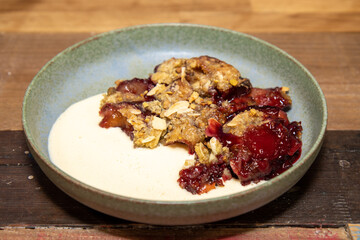 A plate of delicious plum and blackberry crumble on a wooden kitchen table or work top