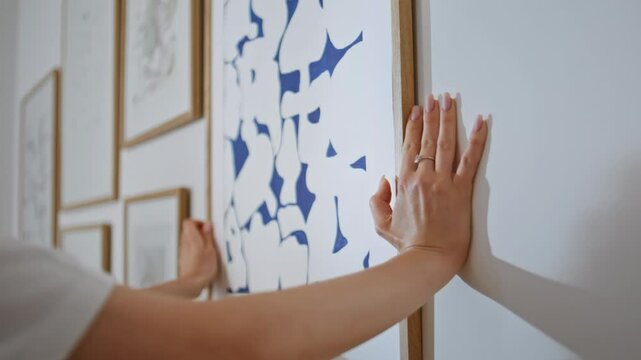 Hands correcting frame paintings on white wall modern apartment closeup. 
