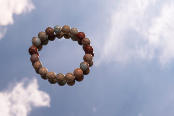 Bracelet made of natural stone against the sky with clouds. Space for text. Moonstone texture. High...