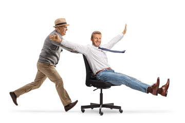 Elderly man pushing a young businessman seated in an office chair