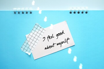 White note on blue background with handwritten text  I FEEL GOOD ABOUT MYSELF - Positive...