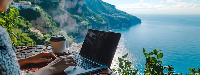 A person working on their laptop with coffee, overlooking the sea
