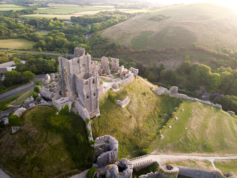 Aerial view of the historic ruins of Corfe Castle on a hill surrounded by scenic greenery and trees, Wareham, United Kingdom.