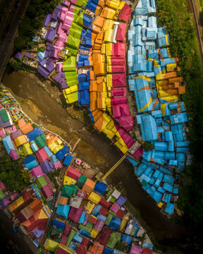 Aerial view of colorful houses and a river with a bridge in a vibrant neighborhood, Blimbing, East Java, Indonesia.