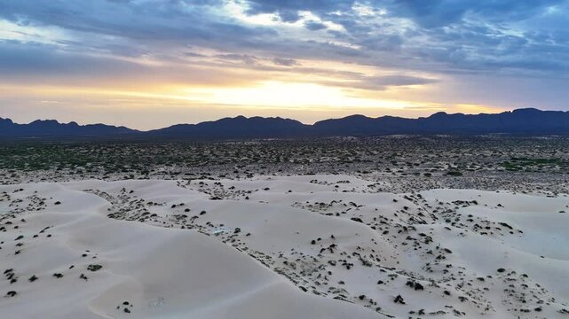 Aerial view of tranquil desert dunes under a serene sunset sky with rugged mountains in the background, Ciudad Juarez, Mexico.