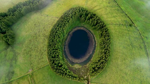 Aerial view of the beautiful Lagoa Pau Pique surrounded by lush forest and trees, Capelas, Portugal.