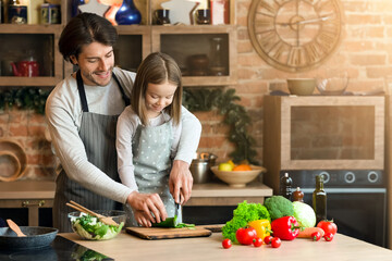 Caring father teaching his adorable daughter how to cook healthy food, cutting vegetables together, free space