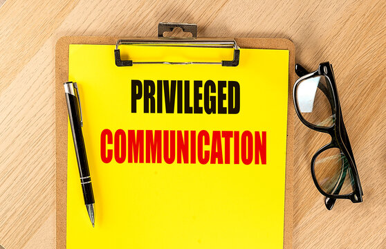  Clipboard with privileged communication text, pen, and glasses on a wooden desk