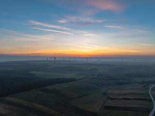 Aerial view of serene sunrise over expansive fields with wind turbines, Matzen-Raggendorf, Austria.