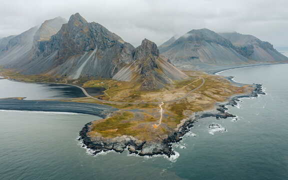 Aerial view of rugged coastline and majestic mountains under a cloudy sky, Hvalnes, Iceland.