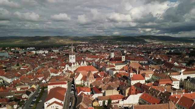 Stunning aerial view of a picturesque town of Sibiu, Romania with a church spire, red rooftops, and rolling hills in the background. Catedrala Evanghelică "Sf&acirc;nta Maria"