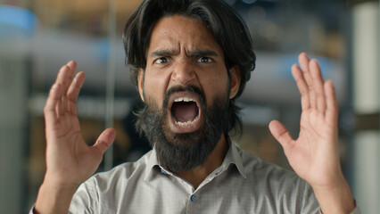 Close-up emotional angry aggressive furious displeased stressful irritated mad Indian bearded man guy shouting screaming yelling swearing shout scream looking at camera stressed male portrait indoors