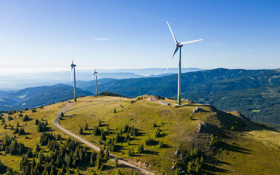 Aerial view of wind turbines on a mountain ridge with a sunny sky and scenic landscape, Weinebene, Austria.