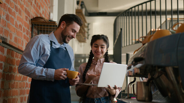 Diverse positive man woman cafeteria employees small business owners cafe manager waiter discussing working schedule on laptop developing new strategy talking about work plan restaurant staff meeting