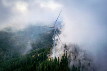 Aerial view of majestic mountains with wind turbines surrounded by clouds and forest, Voitsberg, Austria.