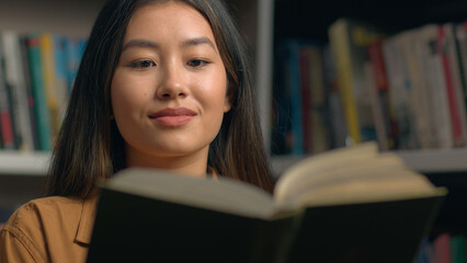 Focused Asian woman girl student ethnic female bookworm reader reading book in university library preparing for college exam studying literature enjoy read textbook education knowledge hobby concept