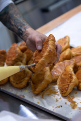 Close-up side view of cook filling fresh baked croissant with custard using icing bag in professional bakery kitchen. Soft focus. Pastry preparation  theme.