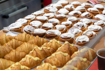 Close-up side view of various fresh baked puff pastry items (croissants with different fillings and cinnamon rolls) on baking trays on professional kitchen table. Soft focus. Food background.