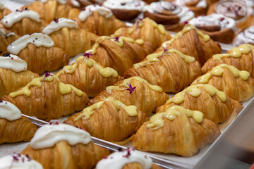 Close-up side view of various fresh baked puff pastry items (croissants with different fillings with edible flowers and cinnamon rolls) on baking tray on professional kitchen table. Food background.