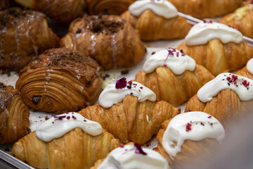 Close-up side view of various fresh baked puff pastry items (croissants with different fillings) on baking tray on professional kitchen table. Soft focus. copy space. Food background theme.