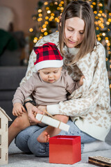 A beautiful little blond boy of 1 year old is sitting with his mother on the background of a Christmas tree. The concept of celebrating Christmas and New Year.