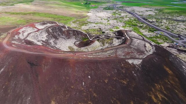 Aerial view of a majestic volcanic crater surrounded by rugged terrain and a vibrant pathway, Grabrok, Iceland.