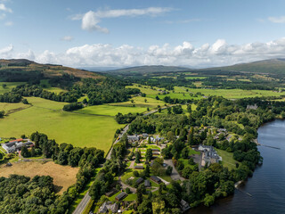 Aerial view of tranquil Loch Lomond surrounded by lush hills and picturesque village, Trossachs National Park, United Kingdom.