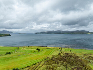 Aerial view of Loch Sligachan surrounded by majestic mountains and green fields under a dramatic cloudy sky, Isle of Skye, United Kingdom.