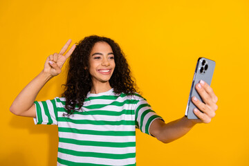 Photo of pretty young girl phone selfie v-sign wear striped t-shirt isolated on yellow color background