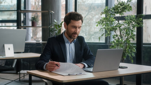 Successful busy Caucasian business man businessman male office employee accountant manager employer developer entrepreneur leader do accounting writing notes enter data in computer working on laptop