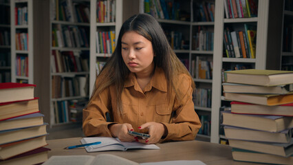 Sad frustrated stressed asian woman girl in university library checking email reading bad news on...