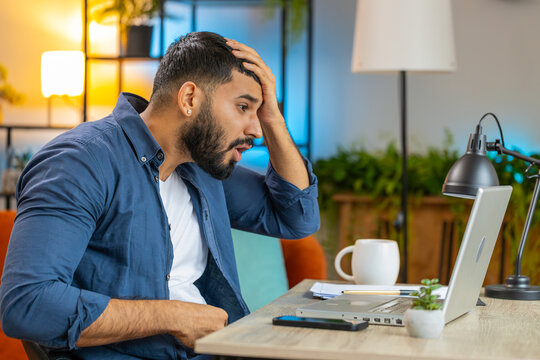 Angry furious Hispanic man freelancer using laptop while working at home office having nervous breakdown at work, stress management, mental distress problems, losing temper, reaction on failure.