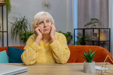 Portrait of sad stressed senior grandmother woman sitting at home looks pensive thinks over life...