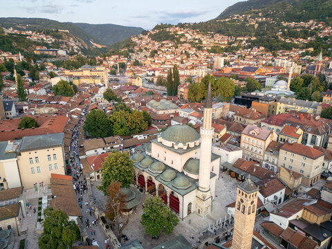 Aerial view of the historic Bascarsija neighborhood with the iconic Gazi Husrev-beg Mosque amidst vibrant rooftops and scenic mountains, Sarajevo, Bosnia and Herzegovina.