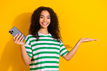 Portrait of nice young girl hold phone empty space wear striped t-shirt isolated on yellow color background