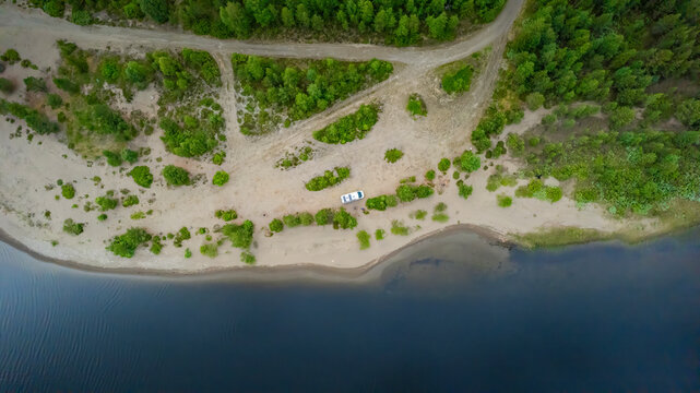 Aerial view of a tranquil lake surrounded by a serene forest and a campervan on a secluded road, Sorsele, Sweden.