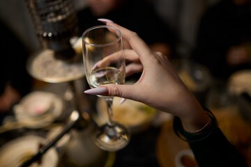 A woman holds a cocktail in her hand, with her fingers wrapped around the glass