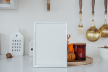 Simple white frame positioned on a kitchen counter with seasonal decorations and utensils in view