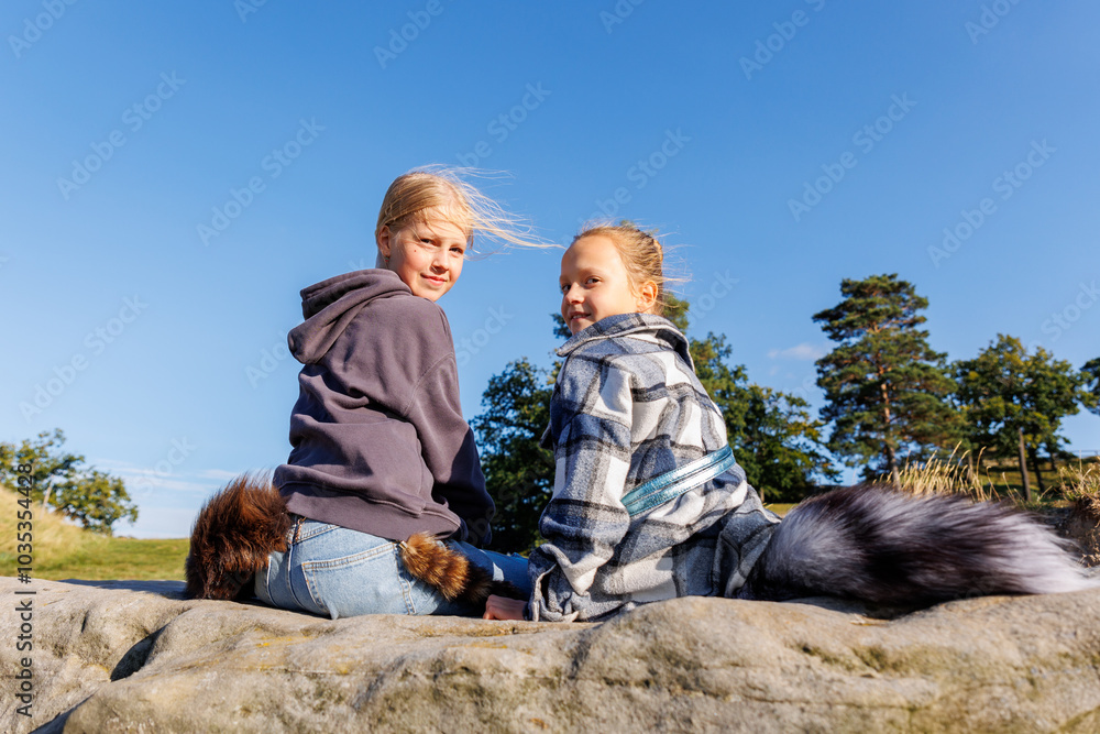 Wall mural back view two cute little girls friends wearing casual hoodies plaid jackets and attached fox fur ta