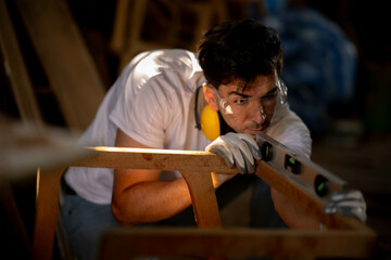 Portrait of Young White carpenter man holding tablet  checking  furniture looking at  measure peice of workintensingly at work site.