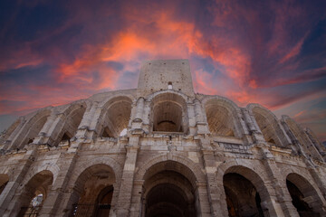 The Arles Roman Amphitheater stands against a fiery sky, reflecting the grandeur of its ancient past. This iconic structure symbolizes the timelessness of Roman engineering and history.