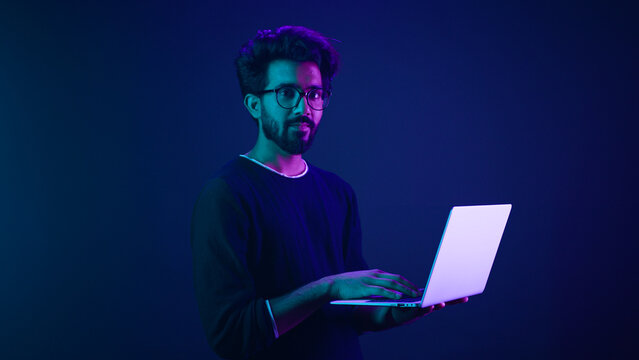 Arabian Indian man guy male programmer coder employer freelancer working using internet computer developer businessman business guy gamer hold laptop computer work in violet neon background network