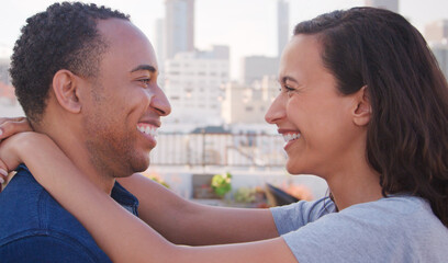 Portrait Of Romantic Couple Looking At Each Other On Rooftop Terrace With City Skyline In Background