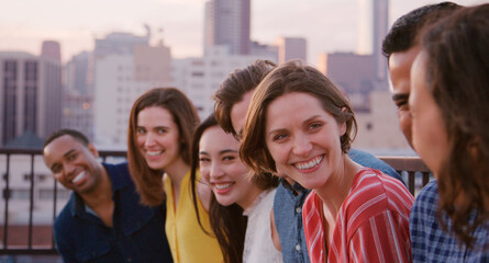 Group Of Friends Standing In A Line On Rooftop Terrace For Party With City Skyline In Background