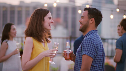 Friends Gathered On Rooftop Terrace For Evening Drinks Party With City Skyline In Background 