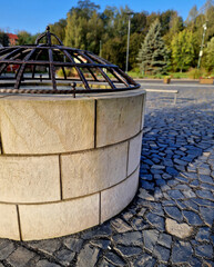 tone round fountain with a protective grid of twisted prisms. forged steel bars go spiraled at the top. around the well there is a retaining wall and a lawn. protection against falling into the depth
