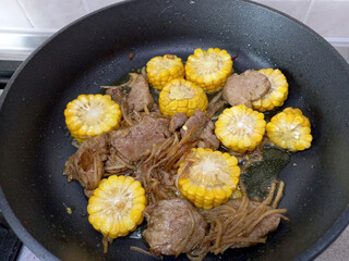 Corn, potato strips and meat are fried in a frying pan